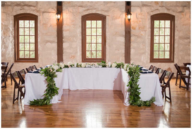 Head Table inside Stone Hall of Texas Old Town Wedding Reception covered in floral garland by Wow Factor Floral in cream