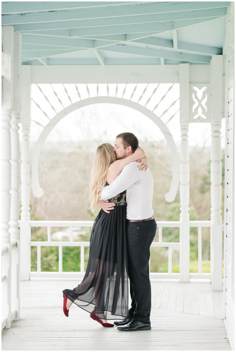 Groom picks up bride and spins her in black dress with the white railing of the balcony at Barr Mansion behind them