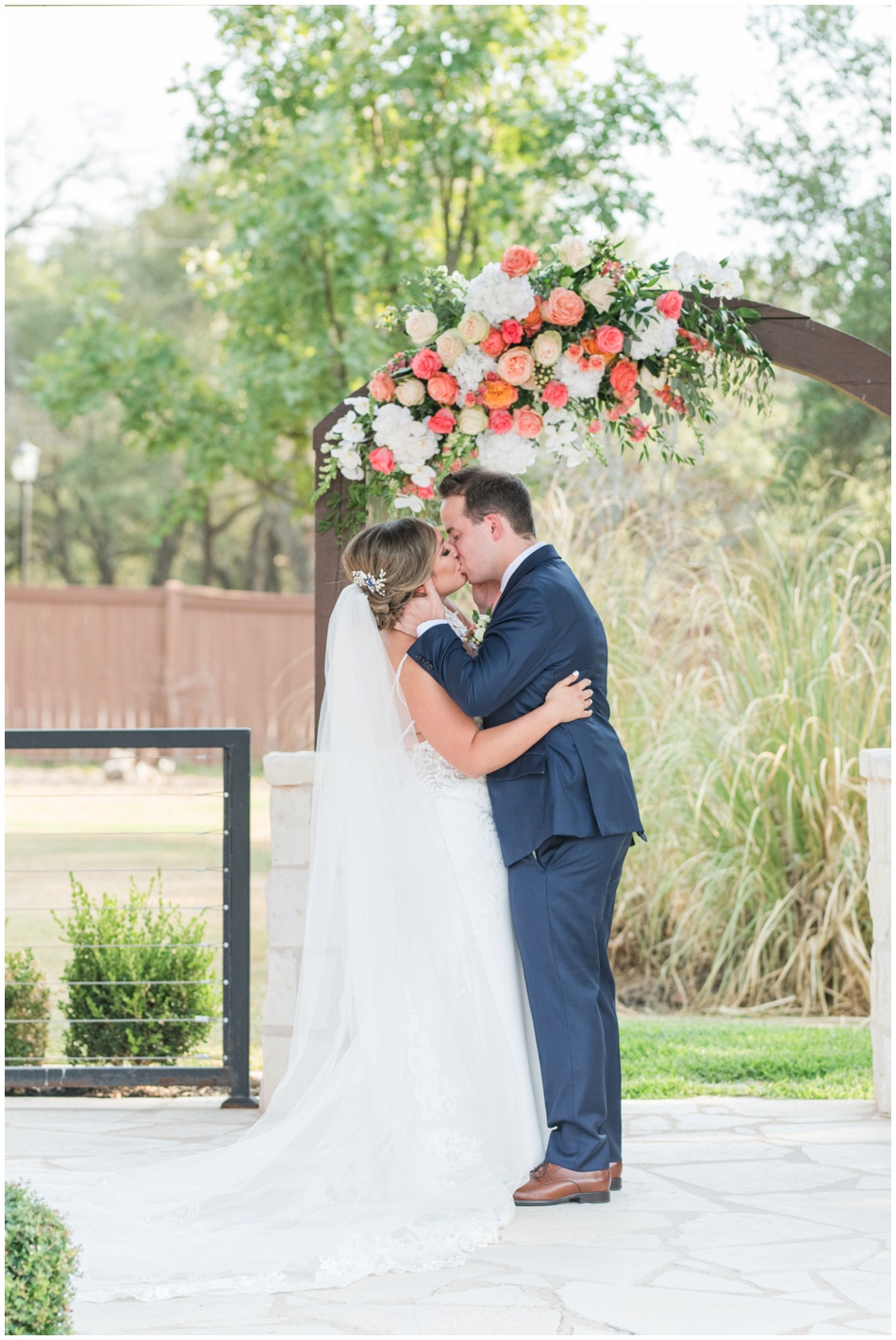First Kiss as husband and wife at The Milestone wedding ceremony with coral flowers on arch