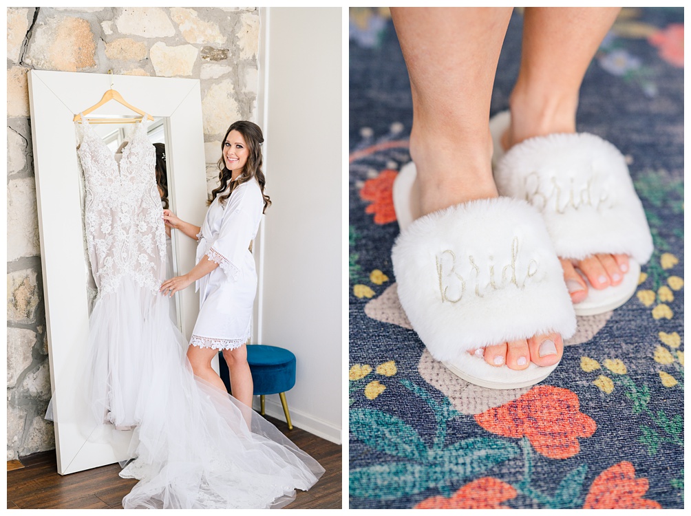 Bridal Suite at Pecan Springs Ranch: Wedding Dress hangs from mirror as bride smiles at the camera in white slippers that say bride