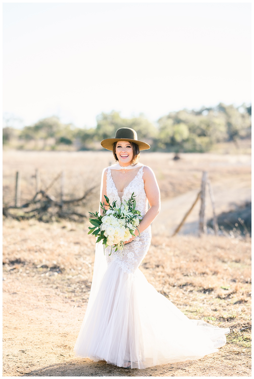 Bridal Portraits at Pecan Springs Ranch; Bride holds white and green wedding bouquet while wearing a bridal cape and a green felt hat