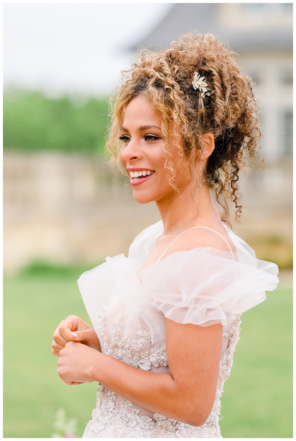 Close-up of a smiling bride with curly hair styled half-up and soft tulle sleeves, showing off the hand-beaded bodice of her whimsical wedding dress during her Austin bridal session.