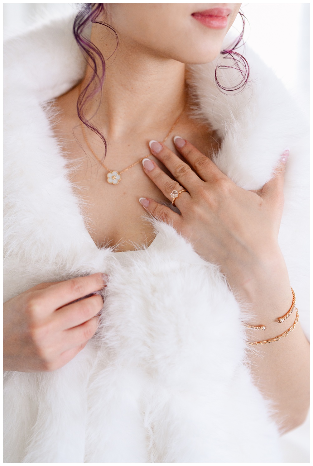 Detail shot of a bride’s hand resting on a faux fur wrap, showing a floral gold necklace, engagement ring, and gold bracelet for a romantic winter wedding look.