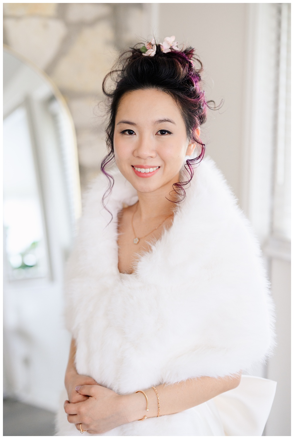 Bride smiles in a cozy white faux fur wrap with blush and floral hair accents, styled for a winter bridal session with a romantic and elegant vibe at Pecan Springs Ranch.