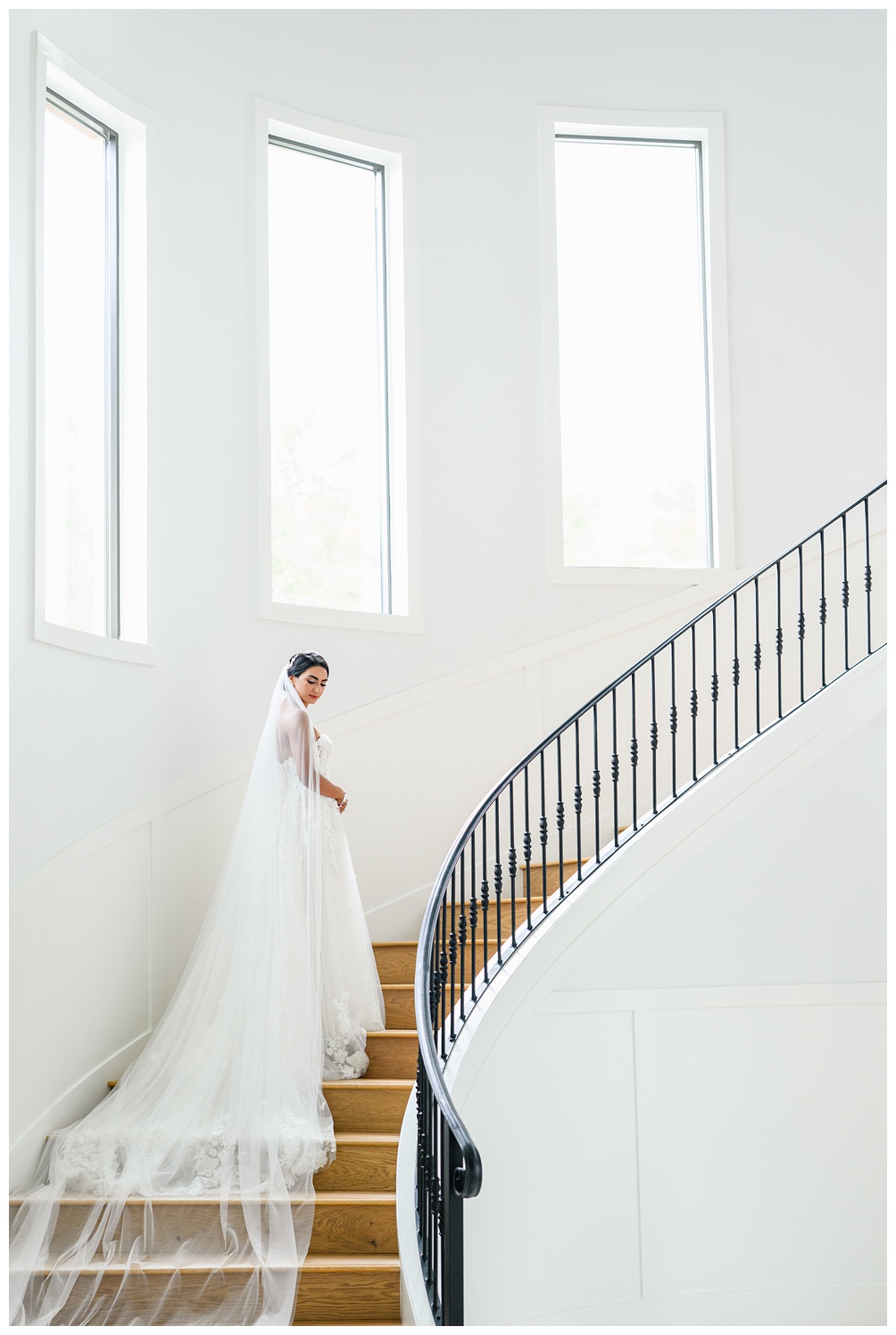 Bride stands on a sweeping staircase in a timeless wedding gown with a full train, captured during her elegant indoor Austin bridal session.