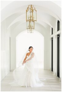 Bride sits in a bright white hallway at the Preserve at Canyon Lake with arched ceilings wearing a romantic strapless gown and veil during her Austin bridal photoshoot with Mylah Renae Photography.