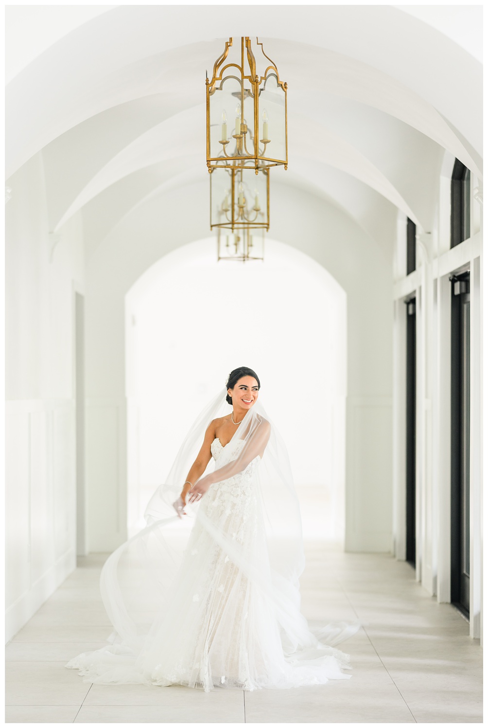 Bride sits in a bright white hallway at the Preserve at Canyon Lake with arched ceilings wearing a romantic strapless gown and veil during her Austin bridal photoshoot with Mylah Renae Photography.