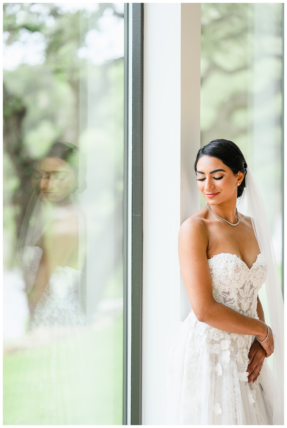 Bride gazes down in front of a bright window wearing a strapless gown with floral appliqué, exuding soft, romantic vibes in her Austin bridal session.