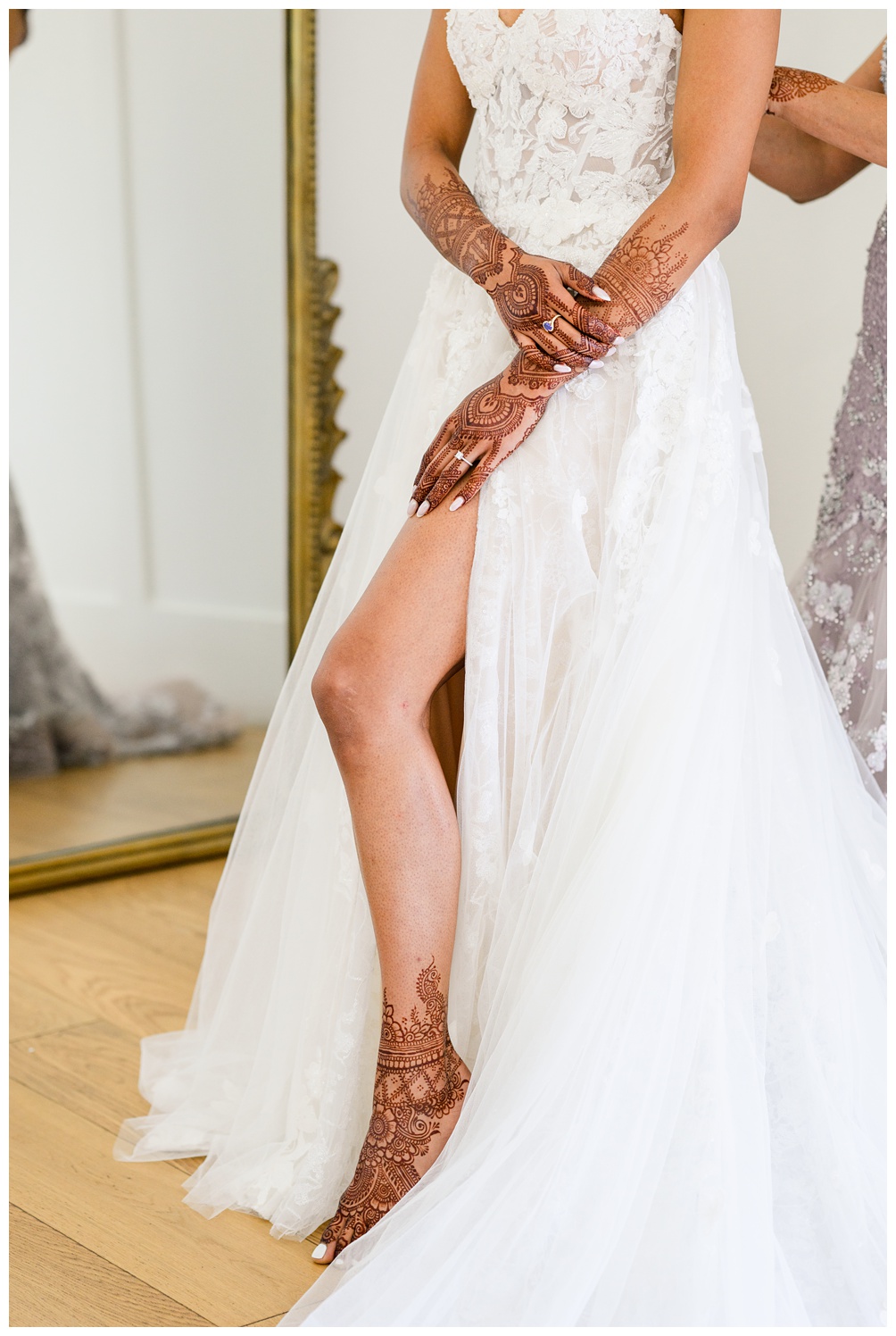 Detail shot of a bride adjusting her gown to reveal a thigh-high slit and strappy heels, captured in front of a gold mirror during an editorial bridal session.